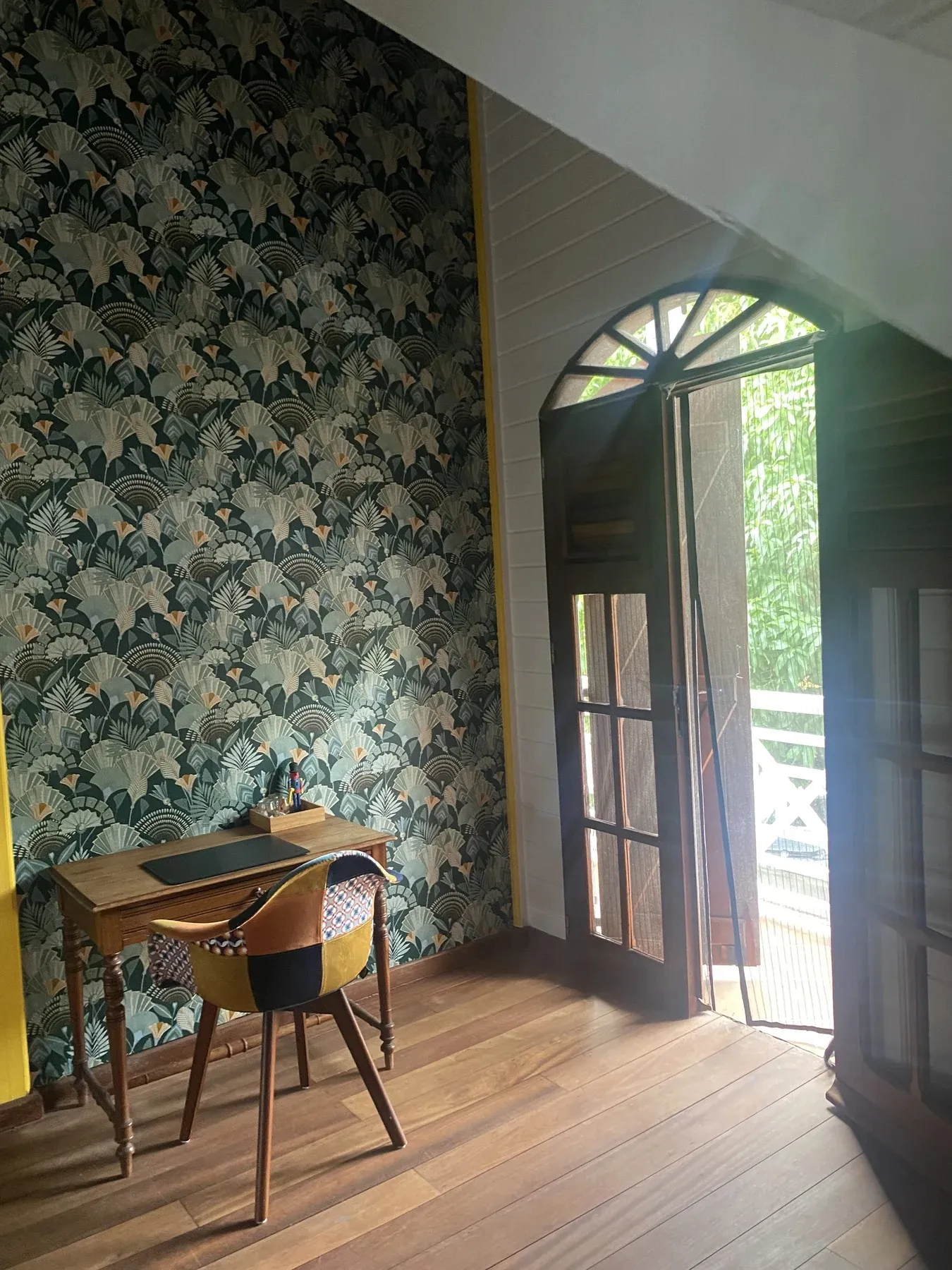 Coin bureau avec papier peint tropical Art déco et porte-fenêtre cintrée ouvrant sur le balcon