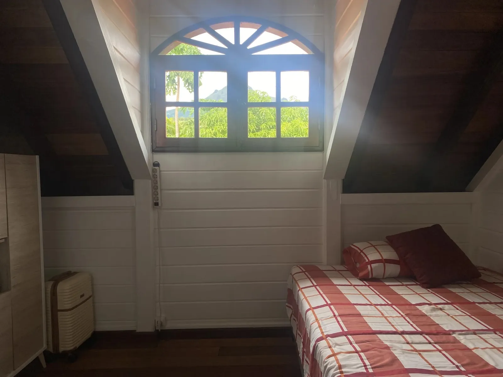 Chambre de la villa avec lit double et fenêtre cintrée ouvrant sur la végétation tropicale