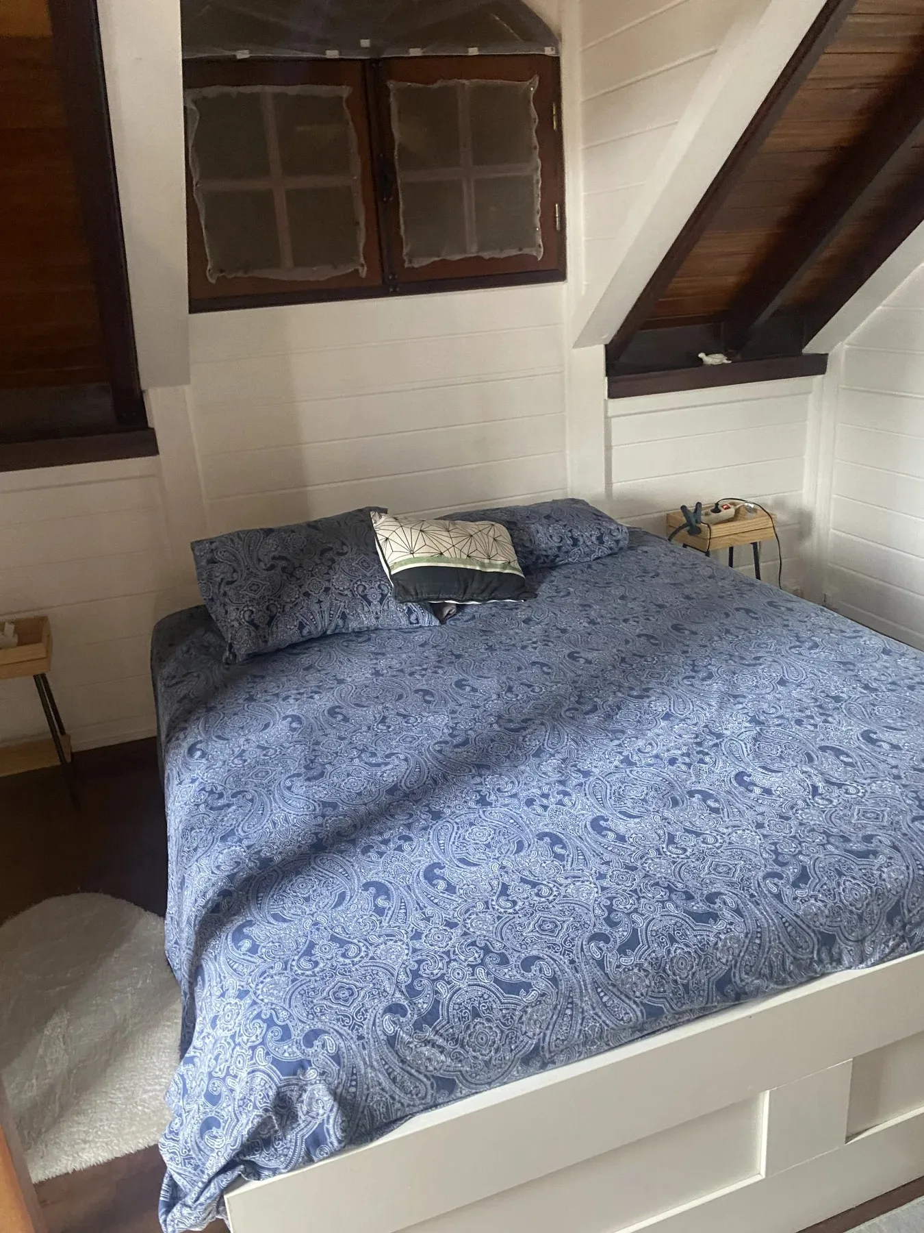 Chambre mansardée de la villa avec grand lit double et murs lambrissés blancs