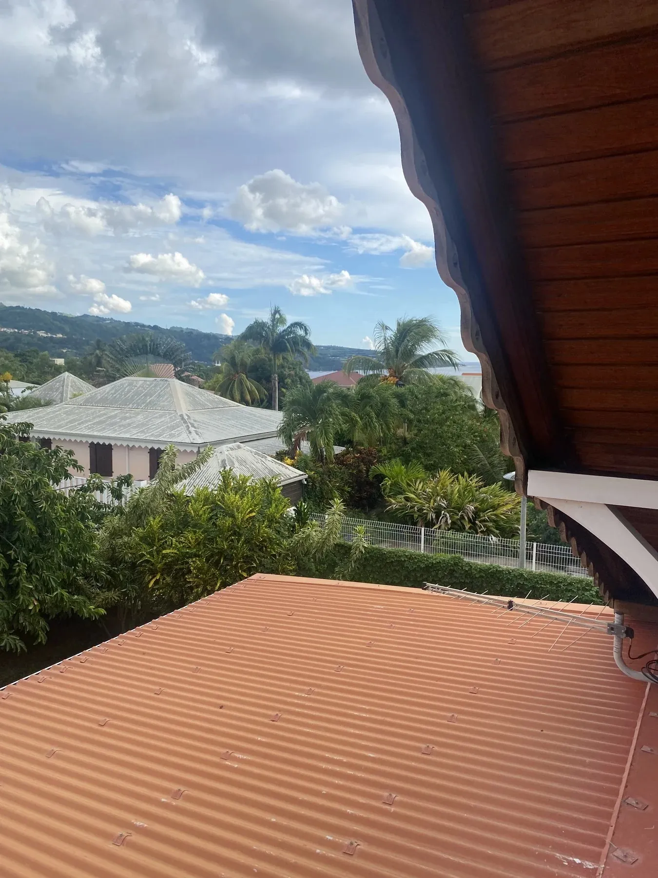 Vue depuis l’étage de la villa sur les toits créoles, la végétation et la mer des Caraïbes